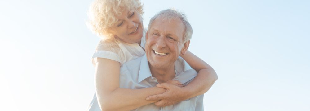 Woman on husbands back with arms around chest, both smiling