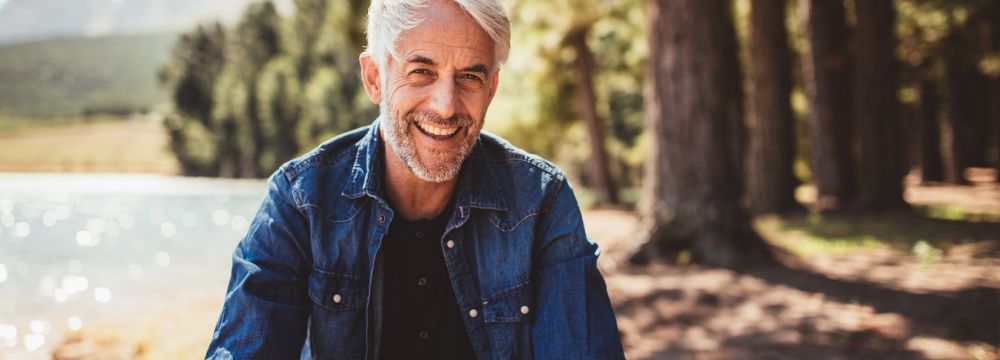 Older man smiling in woods sitting on log