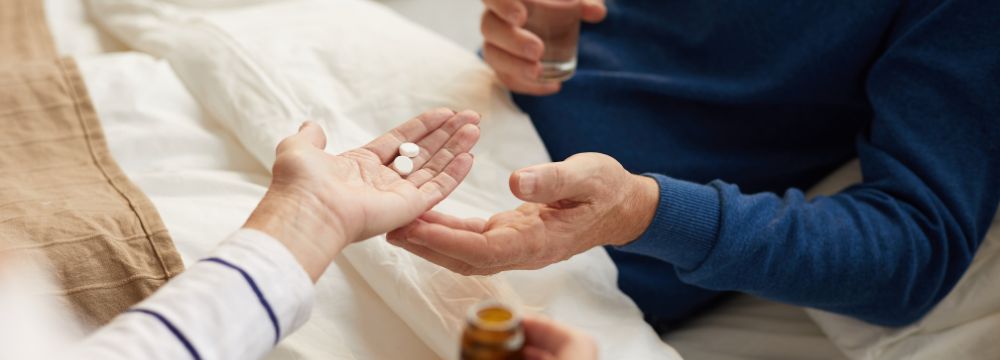 woman handing man meds in bed