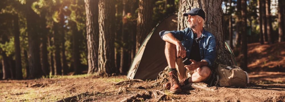 Outdoorsy man pondering while sitting against tree