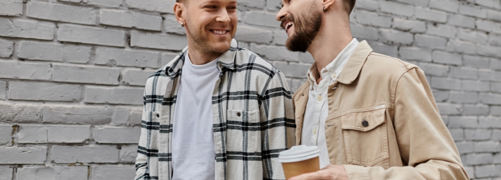 Gay men couple walking, laughing, holding coffee