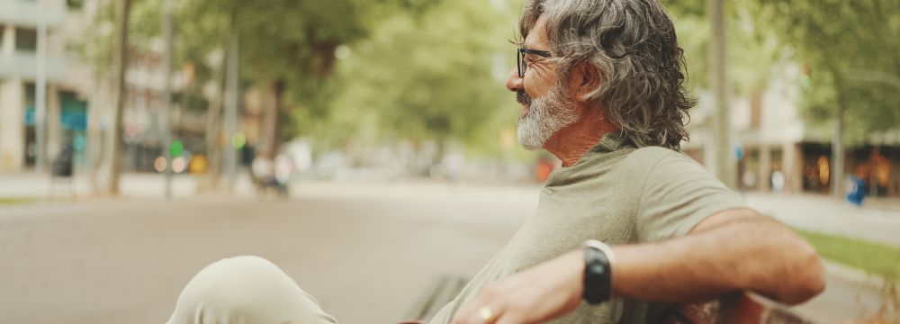 Man sitting on park bench with legs crossed, smiling