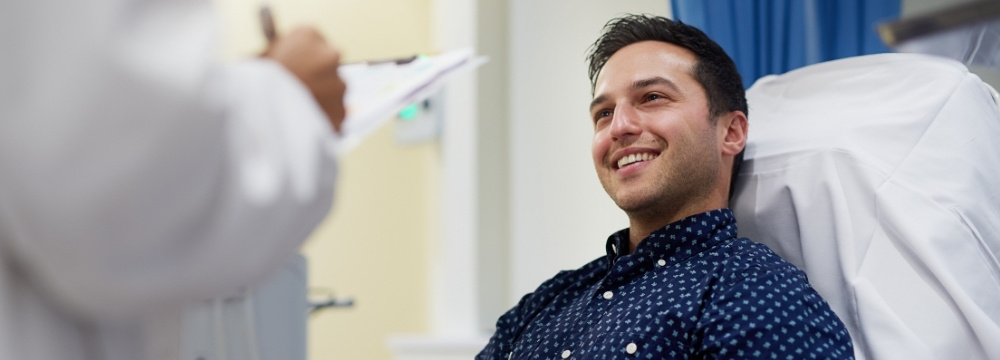 Happy man in doctor's office chair speaking to provider about vasectomy options