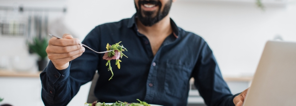 Man smiling while eating healthy lunch, putting fork to mouth